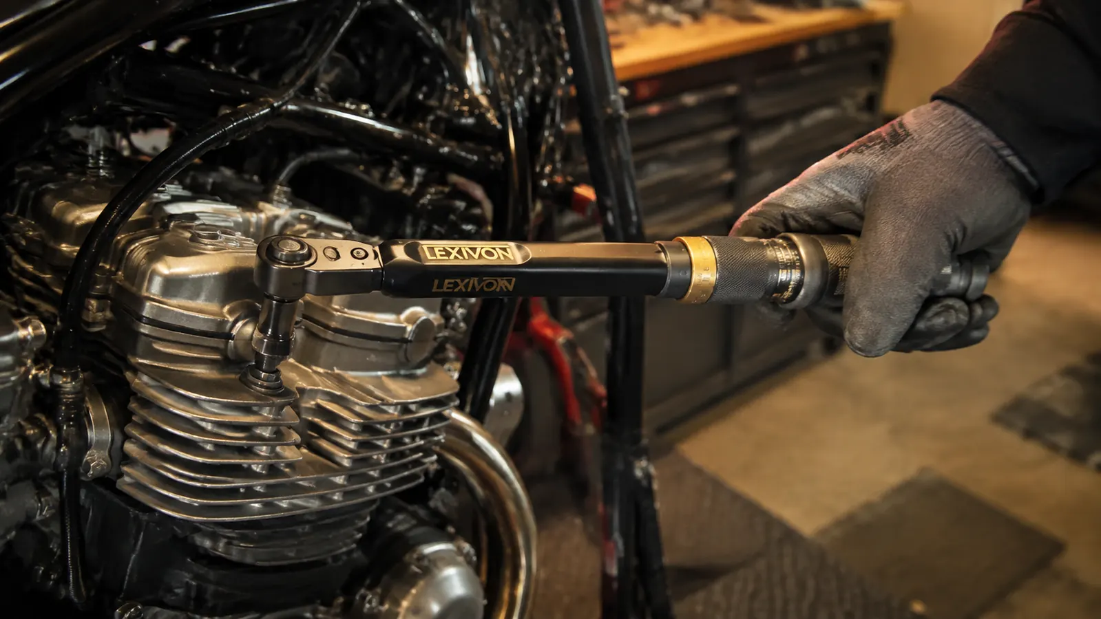 A hand in a work glove pulling a click torque wrench straight on a bike head bolt in a shop